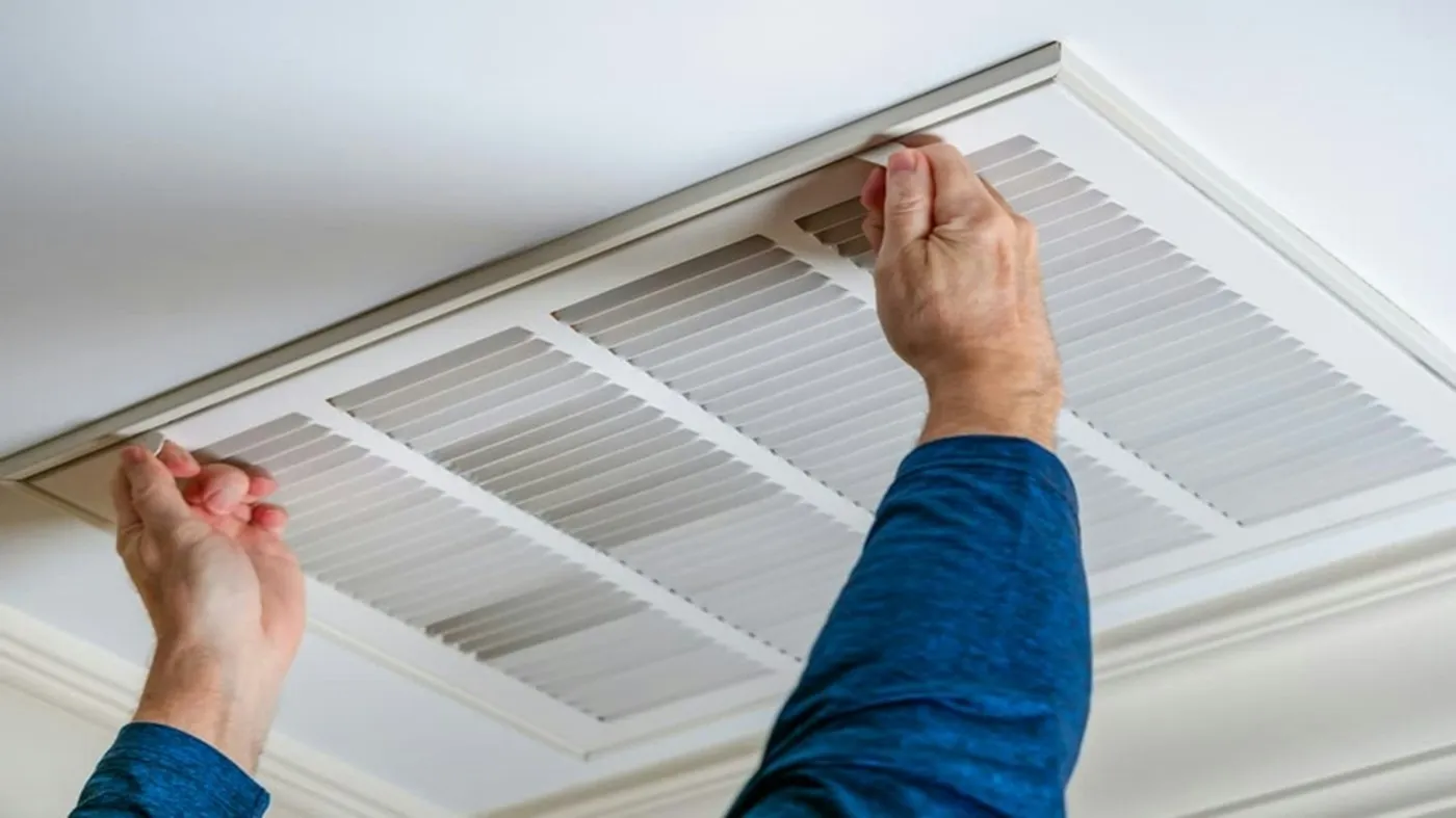 Technician removing a ceiling return air vent cover to clean the ductwork